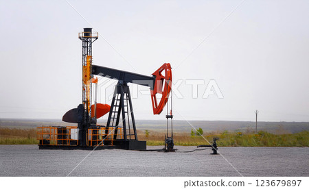 oil pump and oil, depicting a pile of black sand like petroleum residue in the foreground with a blurred miniature oil pump jack, fossil fuel industry, and energy production 123679897