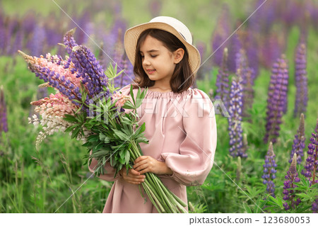 Young caucasian girl in hat holding lupines in blooming field 123680053