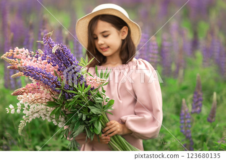 Young caucasian girl in sun hat holding colorful lupine flowers in blooming field 123680135