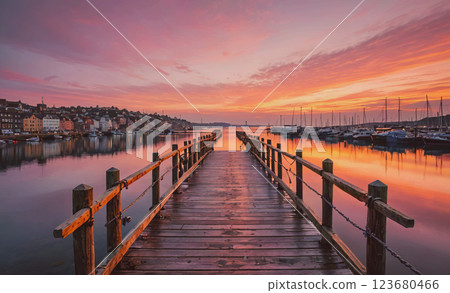 Pier with a beautiful sunset in the background. The water is calm and the sky is filled with orange and pink hues 123680466