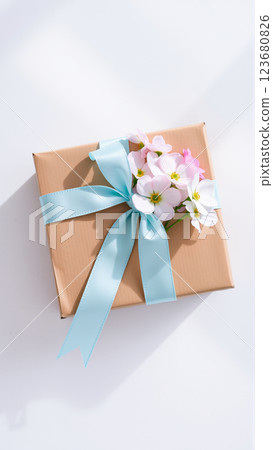 The gift comes in minimalist packaging, decorated with a neutral, calm blue ribbon and flowers symbolizing the arrival of spring. 123680826
