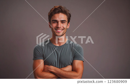 Young man with a smile on his face is wearing a gray shirt and is crossing his arms 123680909