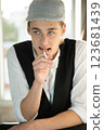 A young man in a cap, a vest, a white shirt, smokes by the window and talks. Bad habits among young people. Young manager. 123681439