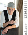 A young man in a cap, a vest, a white shirt, smokes by the window and talks. Bad habits among young people. Young manager. 123681444