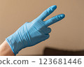A person who is wearing a bright blue glove is making a wellrecognized peace  123681446