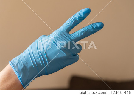 A person who is wearing a bright blue glove is making a wellrecognized peace  A person who is wearing a bright blue glove is making a wellrecognized peace  123681446