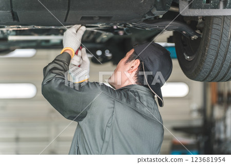 A male mechanic/service technician working, inspecting and servicing the underside of a car that has been lifted A male mechanic/service technician working, inspecting and servicing the underside of a car that has been lifted 123681954