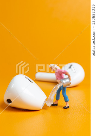 A tiny figurine of a woman appears to clean an oversized earbud 123682319