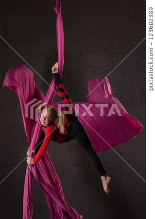 Young girl performs aerial silk exercise against a dark background Young girl performs aerial silk exercise against a dark background 123682389
