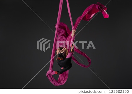 Girl performs aerial silk stunt with pink fabric in studio setting Girl performs aerial silk stunt with pink fabric in studio setting 123682390
