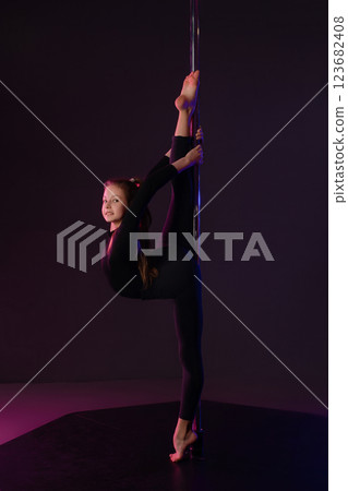 Girl performs impressive pole dance move in a studio setting at night 123682408