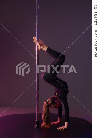 Girl performs a graceful pole dance routine in a studio setting Girl performs a graceful pole dance routine in a studio setting 123682409
