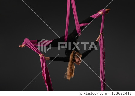 Girl performing aerial silk acrobatics with pink fabric in a dark studio 123682415
