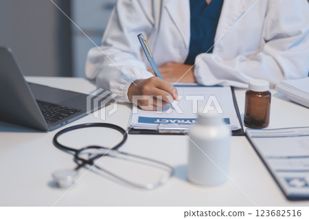 A professional and focused Asian female doctor in scrubs is working and reading medical research on her laptop in her office at a hospital. A professional and focused Asian female doctor in scrubs is working and reading medical research on her laptop in her office at a hospital. 123682516