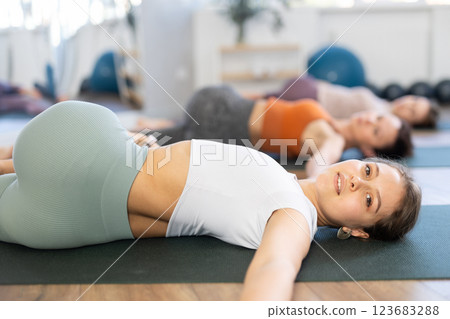 Sporty young woman doing yoga with group in studio, performing hamstring and low back stretching Ardha Pawanmuktasana 123683288
