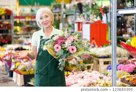 Elderly saleswoman offering bouquet with gerberas and roses at flower market 123683305