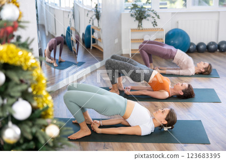 Girl teacher lead yoga lesson for girls and doing chatush padasana in New Year atmosphere. Girl teacher lead yoga lesson for girls and doing chatush padasana in New Year atmosphere. 123683395