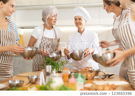 Elderly woman teaching cooking to group of woman Elderly woman teaching cooking to group of woman 123683396