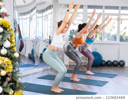 Girl teacher lead yoga lesson for girls and doing chair pose in New Year atmosphere Girl teacher lead yoga lesson for girls and doing chair pose in New Year atmosphere 123683489
