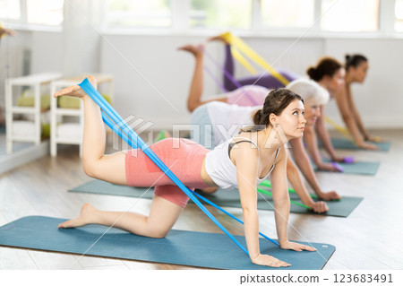 Women on hands and knees doing stretch exercises for legs with resistance band on mats in gym Women on hands and knees doing stretch exercises for legs with resistance band on mats in gym 123683491