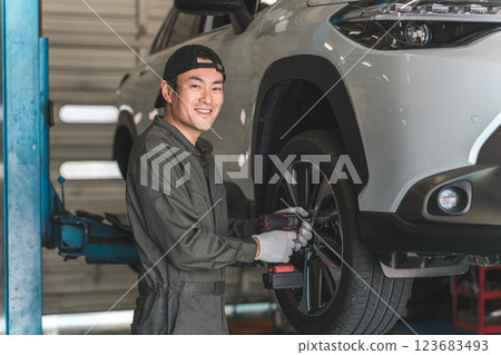 A male mechanic removing and replacing tires on a lifted car (tire change) 123683493