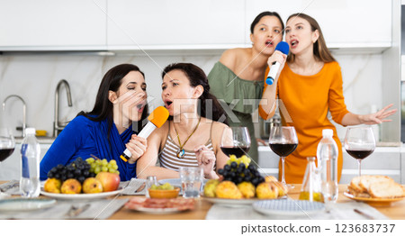 Group of female friends having fun at alcoholic bachelorette party in cozy living room, drinking red wine and singing together at home karaoke 123683737