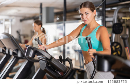 Slender athletic girl during cardio exercises on elliptical simulator in fitness center. 123683753