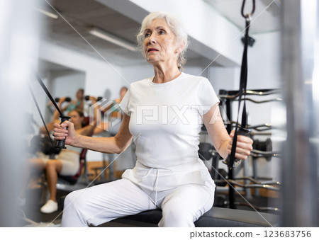 Active athlete mature woman during exercises on crossover exercise machine with loops and weighting Active athlete mature woman during exercises on crossover exercise machine with loops and weighting 123683756