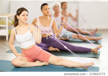 Girl exercising with figure eight resistance band during group pilates class 123683775