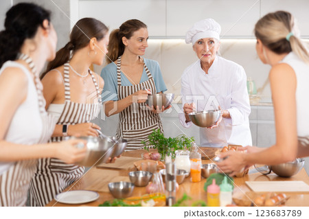 Elderly woman chef with bowl in hands tells women at culinary courses about traditions of cuisine Elderly woman chef with bowl in hands tells women at culinary courses about traditions of cuisine 123683789