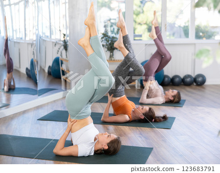 Women perfoming Sarvangasana with Garudasana legs in yoga studio Women perfoming Sarvangasana with Garudasana legs in yoga studio 123683791