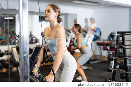 Active athlete young woman during exercises on crossover exercise machine with loops and weighting Active athlete young woman during exercises on crossover exercise machine with loops and weighting 123683843