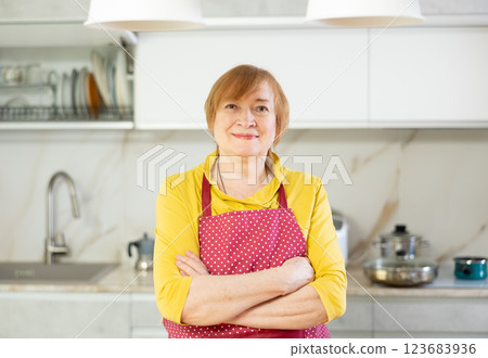 Elderly smiling lady in apron stands in clean kitchen and comes up with menu for lunch 123683936