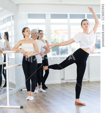 Woman teacher demonstraiting ballet moves in front of women of different ages during group ballet training Woman teacher demonstraiting ballet moves in front of women of different ages during group ballet training 123683942
