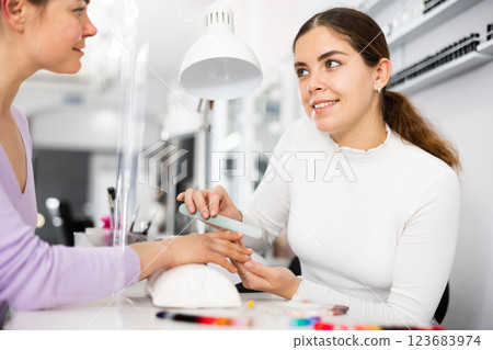 Friendly manicurist files the nails of a young female client Friendly manicurist files the nails of a young female client 123683974