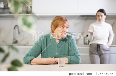 Elderly sad woman sits at table in kitchen and listens to insults.Concept stream of abuse 123683976
