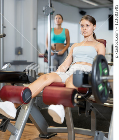 Slender athletic girl work out muscles of legs and thighs on simulator in fitness club Slender athletic girl work out muscles of legs and thighs on simulator in fitness club 123683985
