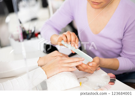 Cropped shot of woman manicurist filing and shaping nails of client 123684001