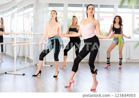 During lesson, girl learn to move and perform dance in heels with women companions During lesson, girl learn to move and perform dance in heels with women companions 123684003