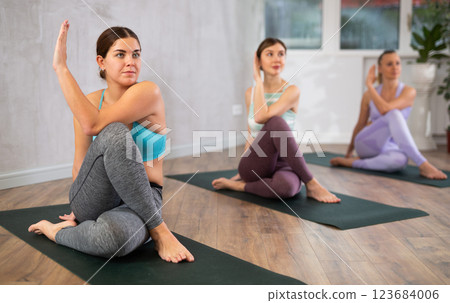 Motivated women in activewear practicing yoga exercises on mats and making Marichyasana or Marichi Pose during workout in studio Motivated women in activewear practicing yoga exercises on mats and making Marichyasana or Marichi Pose during workout in studio 123684006