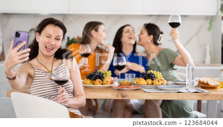 Joyful woman takes selfie against background of happy friends at festive table 123684044