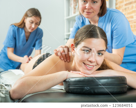 Smiling girl getting relaxing massage from two masseuse 123684051
