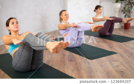 Young focused women doing boat pose in yoga studio Young focused women doing boat pose in yoga studio 123684107