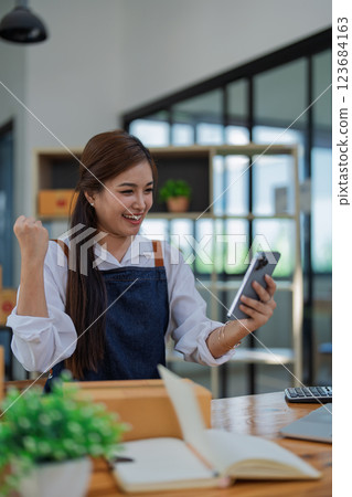 Excited young woman celebrating success while using smartphone to see data delivery products customer profit Selling products of This month Excited young woman celebrating success while using smartphone to see data delivery products customer profit Selling products of This month 123684163