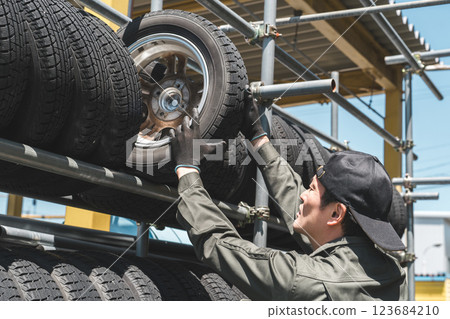 A male mechanic carrying studded tires from a tire rack 123684210
