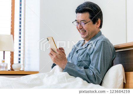 戴眼鏡的中年男子在床上使用智慧型手機 123684259