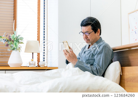 戴眼鏡的中年男子在床上使用智慧型手機 123684260