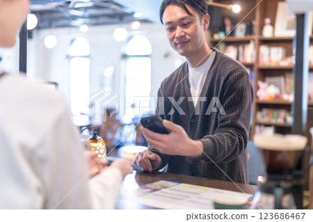 一位男顧客正在用智慧型手機付款，一位女店員 123686467