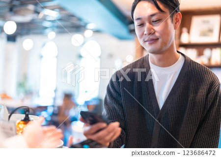 A male customer making a smartphone payment and a female store clerk 123686472