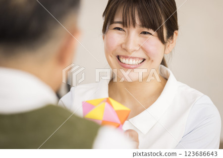 A female caregiver happily receives an origami paper ball from a senior man 123686643